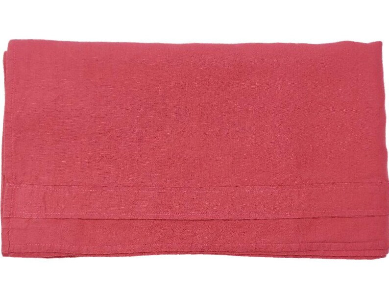 Op de afbeelding: Een gevouwen, effen rode deken. De deken heeft een getextureerd oppervlak en een gevouwen zoom aan de onderkant. De kleur is een levendig, warm rood.