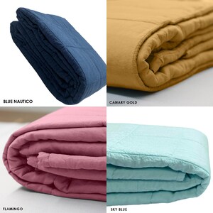 May include: Four folded quilts in different colours: blue, gold, pink, and light blue. The quilts are made of a soft, textured fabric and have a quilted design.
