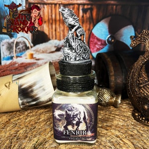 Könnte beinhalten: Ein Glasgefäß mit schwarzem Deckel und einer silbernen Wolfsfigur darauf. Das Gefäß trägt ein Etikett mit der Aufschrift "Fenrir" und "Fabricantes de Brujeria Artesanales by Eitri & Brokkr".