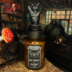 Peut inclure: Une bouteille en verre brun avec un bouchon en forme de chauve-souris noire. L'étiquette indique "Bat Wings" avec une illustration de chauve-souris. La bouteille est décorée d'une corde sombre autour du col. Le thème général est gothique et Halloween.