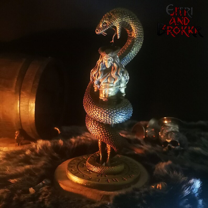 May include: A detailed figurine of a woman wrapped by a snake, with a gold base and runes. The figurine is painted in shades of blue, green, and gold. The text "G&Iacute;TRI AND BROKKR" is visible in the background.
