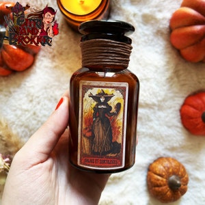 Peut inclure: Une bouteille en verre brun avec un bouchon en liège et une étiquette représentant une sorcière tenant un balai et un panier de citrouilles. L'étiquette indique "Balais et Sortilegues".