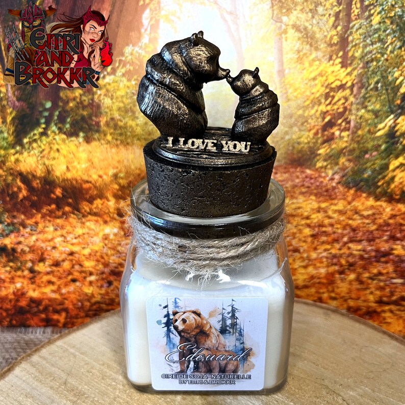 May include: A square glass jar candle with a cork lid. The lid features a bronze-colored sculpture of two bears kissing. The text "I Love You" is engraved on the lid. The candle label features a watercolor illustration of a bear in a forest setting. The text "Edouard" and "Cire de Soja Naturelle by Etti and Brokkr" is printed on the label.