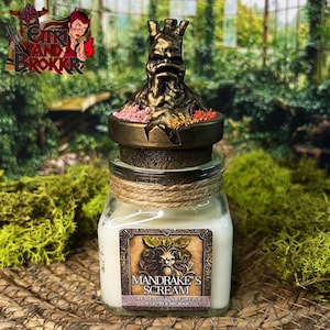 Op de afbeelding: Een kleine glazen pot met een kaars en een gouden deksel met een gebeeldhouwd mandragora-figuur. Het etiket vermeldt "Mandrake's Scream" en "Cire de Soja Naturelle by Eltr & Brokkr".