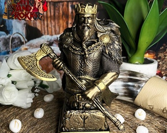 May include: Gold-toned bust of a Viking warrior holding an axe. The warrior is wearing a crown, a chainmail shirt, and a fur cloak. The bust is standing on a base with a rune symbol.