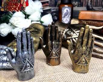 Könnte beinhalten: Drei dekorative handförmige Figuren mit einem allsehenden Auge. Die Hände sind aus Metall und haben eine goldene, silberne und bronzene Oberfläche.
