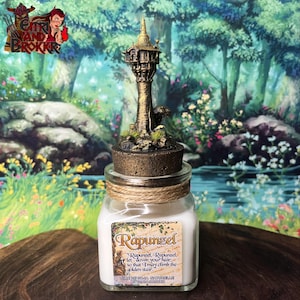 Peut inclure: Une bougie en verre dans un bocal avec un couvercle doré représentant une tour miniature avec une citation du film Disney Rapunzel. La citation dit "Rapunzel, Rapunzel, laisse tomber tes cheveux, afin que je puisse monter l'escalier d'or."