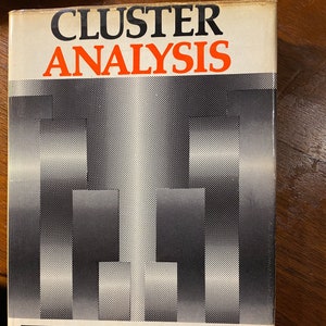 May include: A white book cover with the title "CLUSTER ANALYSIS" in black and red text. The author's name, "BRIAN EVERITT", is printed in gray below a graphic design of black and white squares. The book cover also features the text "SSRC" in gray.
