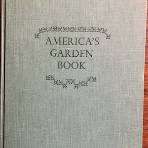 May include: A vintage book titled "America's Garden Book" with a teal cover. The title is in dark green lettering, framed by decorative floral elements. The book's cover has a textured appearance.