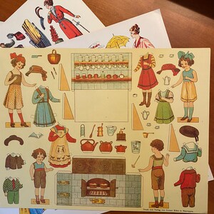 May include: A vintage paper doll set featuring a kitchen scene with a stove, oven, and various kitchen utensils. The set includes several paper dolls dressed in different outfits, including a girl in a red dress, a girl in a green dress, and a boy in a blue and white striped shirt. The paper dolls are ready to be cut out and played with.