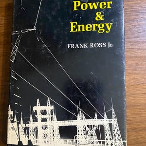 Può includere: Un libro vintage intitolato "THE WORLD OF Power & Energy" di Frank Ross Jr. La copertina è nera con testo bianco e giallo e un'illustrazione bianca di linee elettriche e torri. Il libro è su una superficie di legno.