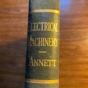 Könnte beinhalten: Ein Vintage-Buch mit dem Titel "Electrical Machinery" von "Annett" mit einem dunkelgrünen Einband und goldenen Lettern.
