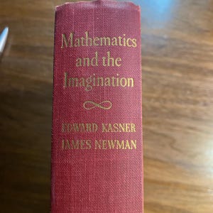 Puede incluir: Un libro de tapa dura rojo con el título "Mathematics and the Imagination" en letras doradas. Los autores, Edward Kasner y James Newman, aparecen debajo del título.