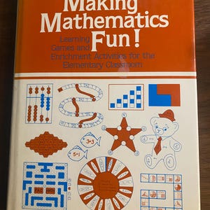 May include: A white softcover book titled Making Mathematics Fun! by Carol Ann Knitzer. The cover features orange text and horizontal stripes, with various illustrations including an abacus, a star, a bear, and game boards with math problems.