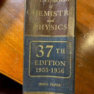 May include: A blue hardcover book titled "Handbook of Chemistry and Physics" with gold lettering. The book is the 37th edition and was published in 1955-1956. It is printed on India paper and published by Chemical Rubber Publishing Co.