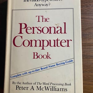 Può includere: Un libro vintage intitolato "The Personal Computer Book" di Peter A. McWilliams. La copertina è bianco sporco con scritte color marrone e uno striscione blu che recita "Complete with up-to-date Brand Name Buying Guide."