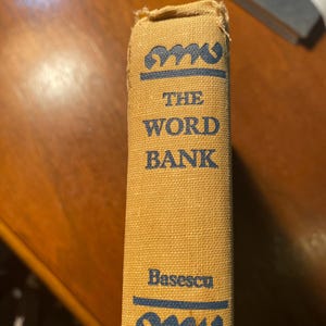 May include: A tan book with the title "The Word Bank" by Basescu. The book has a blue decorative design on the top and bottom of the spine.