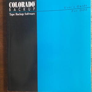 May include: A user's guide for DOS software. The cover is divided into black and blue sections. The black section has the words "COLORADO BACKUP" and "Tape Backup Software" in white text. The blue section has the words "User's Guide For DOS".