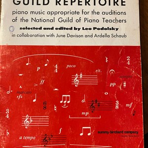 May include: A red cover of a music book titled "Guild Repertoire" with the text "piano music appropriate for the auditions of the National Guild of Piano Teachers" and "selected and edited by Leo Podolsky" in collaboration with June Davison and Ardella Schaub. The cover also includes musical notation.