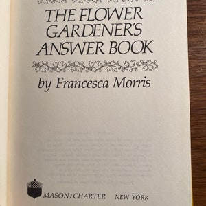 May include: The cover of a book titled "The Flower Gardener's Answer Book" by Francesca Morris. The book cover is white with black text and a decorative border of leaves. The publisher's name, Mason/Charter, is printed in black at the bottom of the cover.