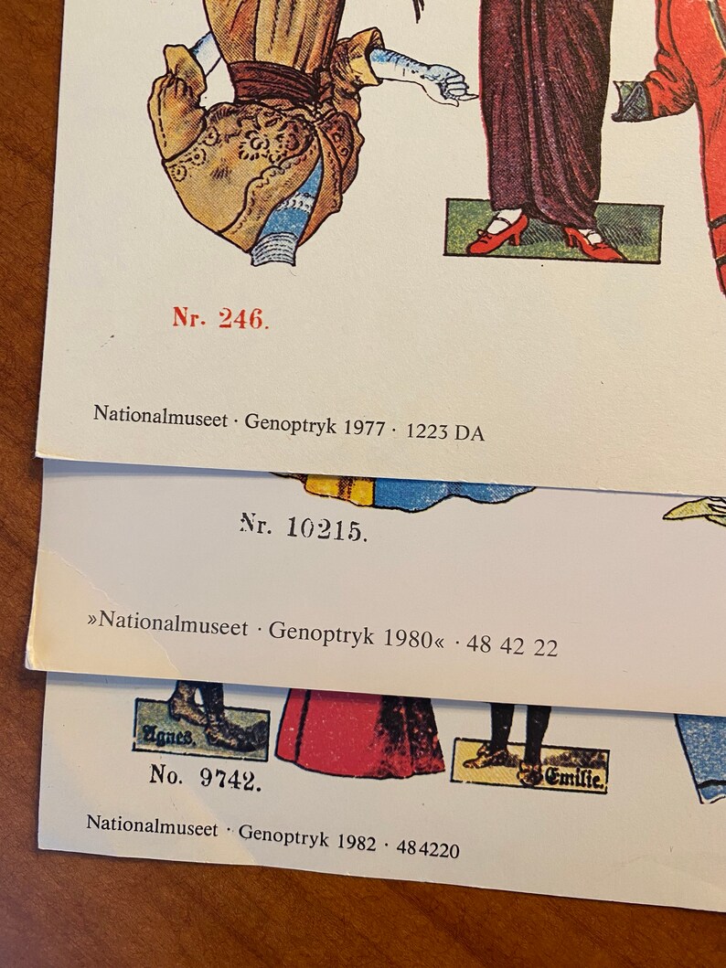 May include: Three paper dolls with text that reads "Nr. 246. Nationalmuseet Genoptryk 1977. 1223 DA", "Nr. 10215. >>Nationalmuseet Genoptryk 1980<< - 48 42 22", and "No. 9742. Nationalmuseet Genoptryk 1982. 484220".