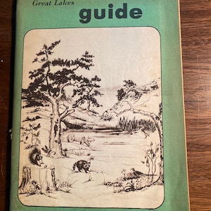 Könnte beinhalten: Ein Vintage-Naturführer in Grün und Braun mit dem Titel "nature guide" und "Great Lakes" auf dem Cover. Das Cover zeigt eine Schwarzweißillustration einer Waldszene mit einem See, Bäumen und Tieren.