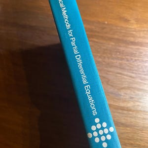 May include: A teal book spine with the title "Numerical Methods for Partial Differential Equations" in white text. A cluster of white dots is near the bottom. The author's name, Ames, is also visible.