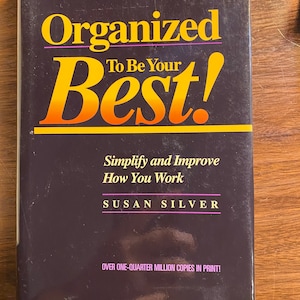 以下が含まれることがあります： スザン・シルバー著「Organized To Be Your Best!」というタイトルの紫と黒の本。本の表紙は黄色とオレンジのタイトルで、「Simplify and Improve How You Work」という文字が白で書かれている。この本は第4版であり、受賞歴のある「組織の聖書」として紹介されている。