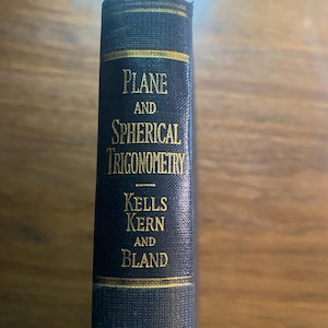 May include: A dark blue hardback book spine with gold lettering that reads Plane and Spherical Trigonometry by Kells, Kern, and Bland. The spine features horizontal gold lines above and below the title and author names on a textured fabric cover.