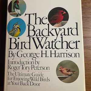 Op de afbeelding: Een hardcover boek getiteld "The Backyard Bird Watcher" van George H. Harrison. De omslag toont illustraties van vogels in cirkelvormige inzetstukken en de tekst "The Ultimate Guide for Enjoying Wild Birds at Your Back Door."