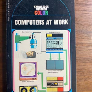 May include: A vintage book cover titled "Computers at Work" with the text "Knowledge Through Color." The cover features illustrations of a gamma camera, analog computer, and color TV monitor. The author's name is John O. E. Clark.