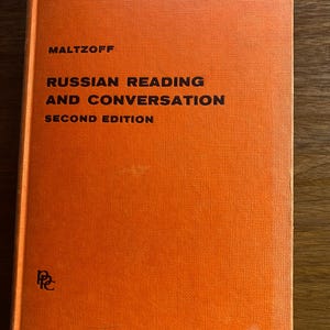 Pode incluir: Um livro de capa dura com uma capa laranja brilhante e texturizada. A capa apresenta um texto em preto que diz MALTZOFF RUSSIAN READING AND CONVERSATION SECOND EDITION. Um pequeno logótipo preto é visível no canto inferior esquerdo.