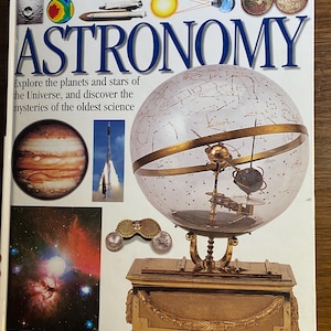 Op de afbeelding: Een hardcover boek getiteld "ASTRONOMY" met een heldere globe en een goudkleurige standaard. De boekomslag bevat afbeeldingen van planeten, een raketlancering en de tekst "Explore the planets and stars of the Universe, and discover the mysteries of the oldest science."