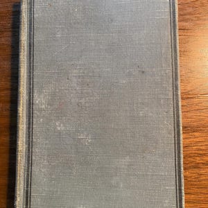 May include: A gray hardcover book with a black border around the cover. The book has a textured fabric cover.