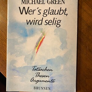 May include: A book cover with a watercolor painting of a rainbow in a blue sky. The title of the book is "Wer's glaubt, wird selig" and the author is "Michael Green". The book is published by "BRUNNEN" and the subtitle is "Tatsachen Thesen Argumente".