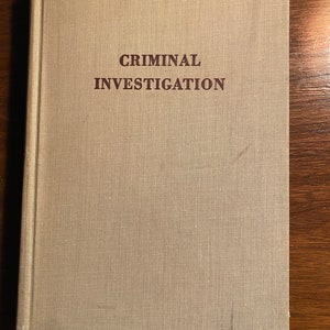 Puede incluir: Un libro beige con el título "CRIMINAL INVESTIGATION" impreso en letras marrones en la portada.