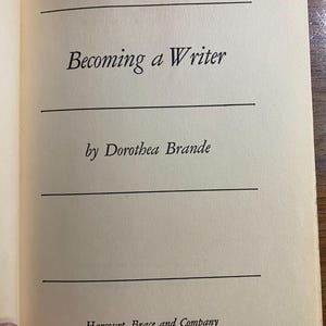 Può includere: Pagina di libro aperta con il titolo "Becoming a Writer" di Dorothea Brande. Pubblicato da Harcourt, Brace and Company, New York. Il testo è in un classico font serif, con linee orizzontali che separano il titolo e il nome dell'autore.