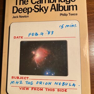 Puede incluir: Un libro titulado "The Cambridge Deep-Sky Album" de Jack Newton y Philip Teece. La portada presenta una fotografía de la Nebulosa de Orión, etiquetada como "M42 The Orion Nebula". La fecha "FEB.4. '83" y "15 MINS." están escritas a mano en la portada.