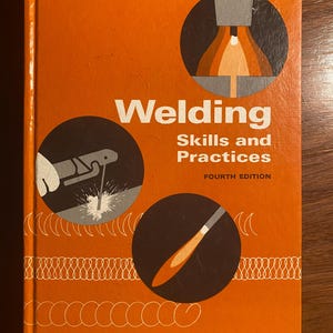 May include: An orange book cover with the title "Welding Skills and Practices, Fourth Edition" and illustrations of welding tools. The book cover also features the authors' names: Giacchino, Weeks, and Brune.