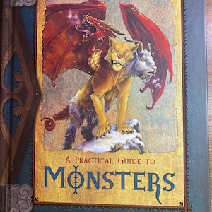 May include: A book cover with a blue background and a gold border. The cover features an illustration of a lion-like creature with a goat head and a dragon's wings. The title of the book is "A Practical Guide to Monsters".