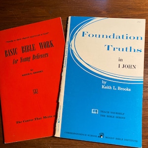 Puede incluir: Dos libros de bolsillo rojos y azules con los títulos "Basic Bible Work for Young Believers" y "Foundation Truths in I John" de Keith L. Brooks. Ambos libros forman parte de la serie "Teach Yourself the Bible Series" del Moody Bible Institute.
