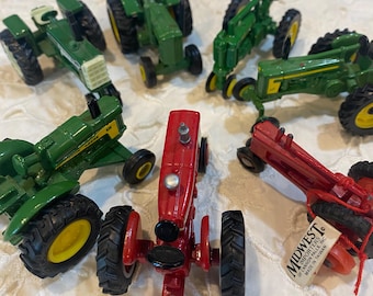 May include: A collection of six miniature die-cast toy tractors in green and red. The green tractors feature yellow wheels and black tyres, while the red tractors have black wheels and tyres. One red tractor has a tag reading MIDWEST IMPORTERS.