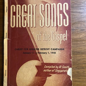 May include: A vintage book cover with the title "GREAT SONGS of the Gospel" in white lettering on a maroon background. The cover also features text for the Christ for Greater Detroit Campaign, January 11 to February 1, 1948, and the author, Al Smith.