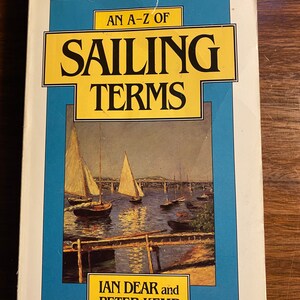 Puede incluir: Una portada de libro con un diseño amarillo y azul. El título es "An A-Z of Sailing Terms" de Ian Dear y Peter Kemp. La portada presenta una pintura de veleros en una masa de agua.