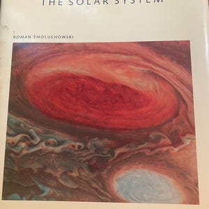 May include: A hardback book titled THE SOLAR SYSTEM by Roman Smoluchowski. The cream-coloured cover features a large, detailed rectangular illustration of the planet Jupiter, highlighting its prominent red spot and swirling orange and white clouds.
