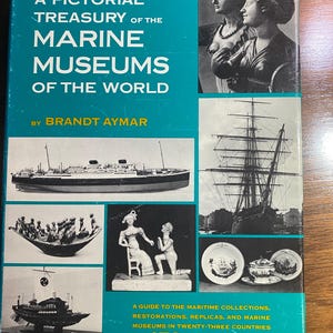 May include: A book titled "A Pictorial Treasury of the Marine Museums of the World" by Brandt Aymar. The cover is teal with images of sculptures, ships, and maritime artifacts. The book contains 470 photographs and a guide to maritime collections.