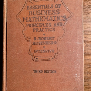 May include: A brown book with the title "Essentials of Business Mathematics Principles and Practice" by R. Robert Rosenberg, Intensive, Third Edition.