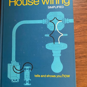 May include: A blue book titled "House Wiring Simplified" by Floyd M. Mix. The cover features yellow text and illustrations of electrical wiring components, including a lightbulb and a switch. The text "tells and shows you how" is also present.