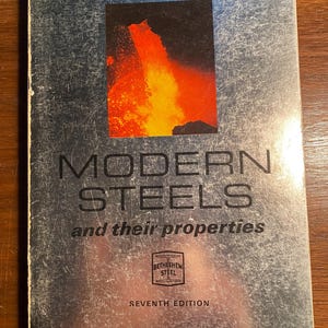 Könnte beinhalten: Ein silberner Buchumschlag mit dem Titel "MODERN STEELS and their properties" in schwarzer Schrift. Der Buchumschlag zeigt außerdem ein Foto eines Vulkanausbruchs und das Logo von Bethlehem Steel.