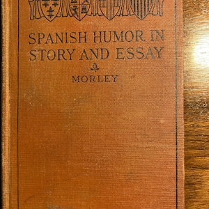 Puede incluir: Un libro marrón con un borde negro y el título "SPANISH HUMOR IN STORY AND ESSAY" de MORLEY.